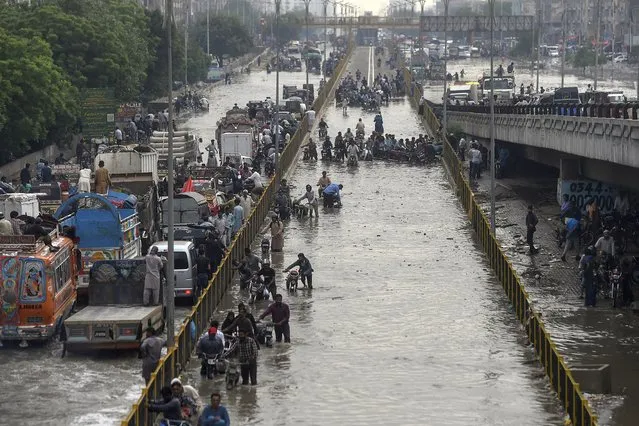 Commuters cross a flooded street after a heavy rainfall in Karachi on September 23, 2021. (Photo by Asif Hassan/AFP Photo)