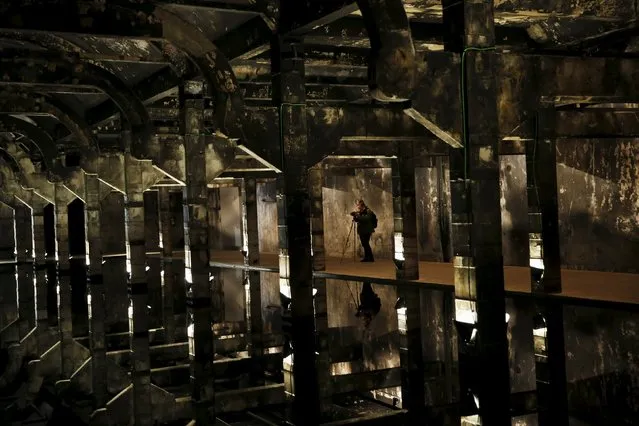 A woman takes pictures of the artwork “Every word is like an unnecessary stain on silence and nothingness” by Spanish artist Eugenio Ampudia at Matadero Madrid culture center in Madrid, Spain, April 28, 2015. A pool of still water reflects the burnt-out beams, walls and ceiling of a burnt-out room. Matadero Madrid, located in an old slaughterhouse and livestock market, is a music, art, design and film center which opened its doors in 2007. (Photo by Susana Vera/Reuters)