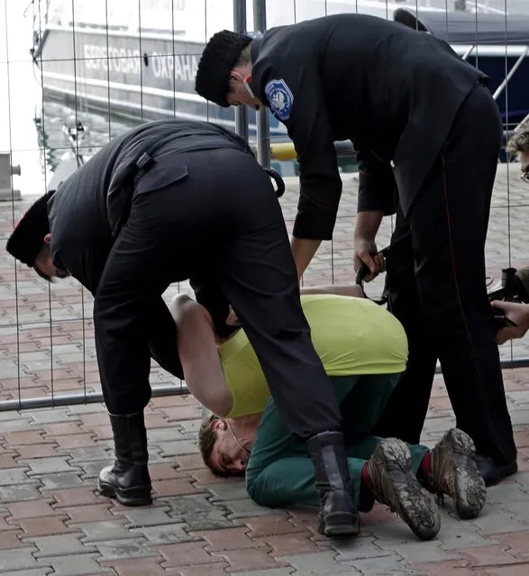 A member of the punk group p*ssy Riot is restrained by Cossack militia after the group tried to perform in Sochi, Russia, on Wednesday, February 19, 2014. The group had gathered in a downtown Sochi restaurant, about 30km (21miles) from where the Winter Olympics are being held. They left the restaurant wearing bright dresses and ski masks and had only been performing for a few seconds when they were set upon by Cossacks. (Photo by Morry Gash/AP Photo)