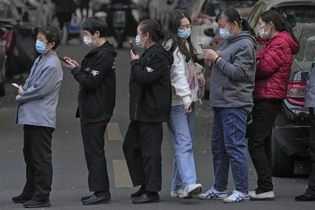 A woman wearing a face mask to help curb the spread of the coronavirus walks through a line of masked service sector women waiting to receive a swab for the COVID-19 test during a mass testing in Beijing, Friday, October 29, 2021, following a spike of the coronavirus in the capital and other provincials. (Photo by Andy Wong/AP Photo)