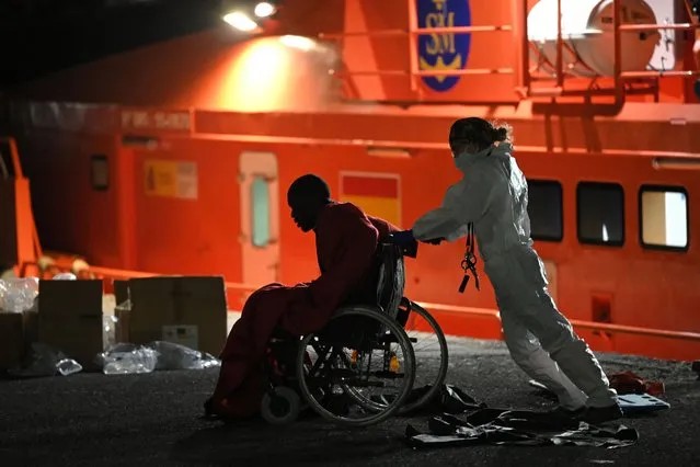An emergency worker helps a migrant on a wheelchair, in the port of Arguineguin, after a rescue operation off the coast of the Canary island of Gran Canaria on November 18, 2021. Migrant crossings from North Africa into Spain have surged this year, with many people risking their lives on dangerous boat journeys across the Mediterranean. Some 16,827 migrants have arrived in the Canaries between January and October, an increase of 44 percent from the same period a year ago, according to Spain's interior ministry. (Photo by Lluis Gene/AFP Photo)