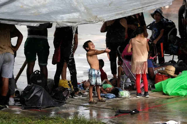 A boy plays with rain water as migrants seek shelter from the rain as they take part in a caravan heading to Mexico City, in Escuintla, Mexico on October 28, 2021. (Photo by Daniel Becerril/Reuters)