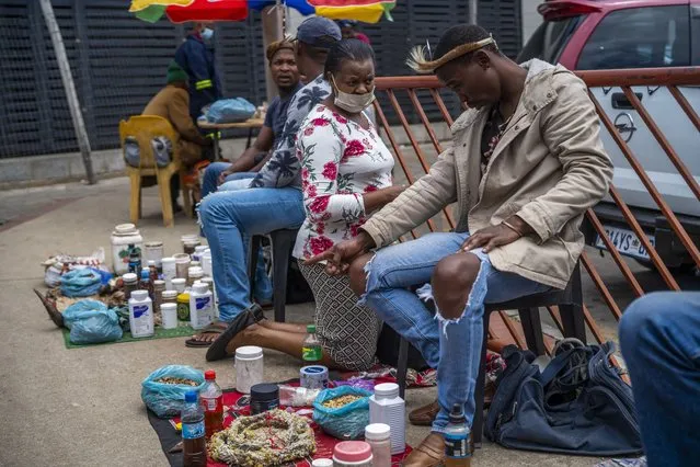 A woman consults a traditional doctor near the Baragwanath taxi rank in Soweto, South Africa, Thursday December 2, 2021. Fearing vaccines, some turn to traditional doctors for COVID-19 remedies. South Africa launched an accelerated vaccination campaign to combat a dramatic rise in confirmed cases of COVID-19 a week after the omicron variant was detected in the country. (Photo by Jerome Delay/AP Photo)