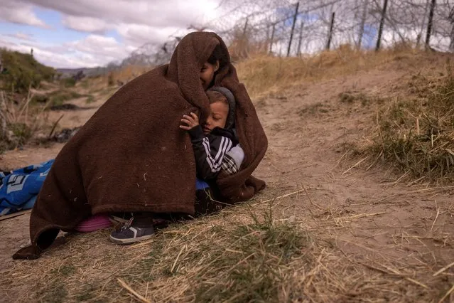 Jolimar, an 18-year-old migrant from Venezuela, shelters her two-year-old son Gail from the cold and blustery weather as they search for an entry point into the U.S. past a fortified fence laden with razor wire along the bank of the Rio Grande river in El Paso, Texas on March 25, 2024. (Photo by Adrees Latif/Reuters)