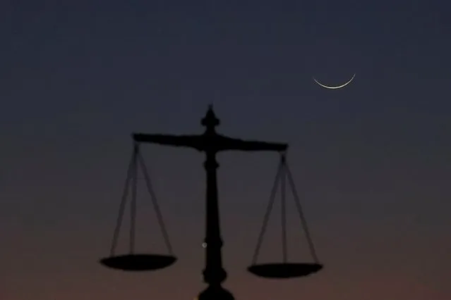 A crescent moon is seen with a monument of balance scale at the Sindh High Court premises, as Muslims attend an evening prayer session called “Tarawih” to mark the holy fasting month of Ramadan in Karachi, Pakistan on March 11, 2024. (Photo by Akhtar Soomro/Reuters)