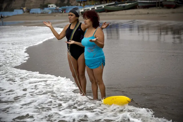 In this May 8, 2015 photo, sisters Zoraida Infante, left, and Graciela Trujillo pray on Fishermen's Beach before therapeutic swimming in the Pacific Ocean in Lima, Peru. Under overcast skies, the bathers practice thalassotherapy, which derives from the Greek “thalasso”, for “sea”, and draws on the ocean's healing properties. (Photo by Rodrigo Abd/AP Photo)