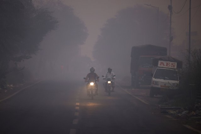 People ride on motorcycles through smoke from burning garbage following a fire at the Ghazipur landfill site, in New Delhi, India on April 22, 2024. (Photo by Adnan Abidi/Reuters)