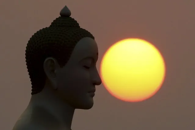 The sun rises next to a Buddha statue while monks and novices gather to receive alms at Wat Phra Dhammakaya temple, in what organizers said was a meeting of over 100,000 monks in Pathum Thani, outside Bangkok, April 22, 2016. (Photo by Jorge Silva/Reuters)
