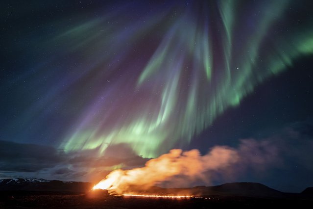 A view of the eruption area with the northern lights dancing in the sky near the town of Grindavik, Iceland, Tuesday April 16, 2024. The volcano in southwestern Iceland that erupted three times in December, January and February, sending lava towards a nearby community, keeps erupting. (Photo by Marco di Marco/AP Photo)