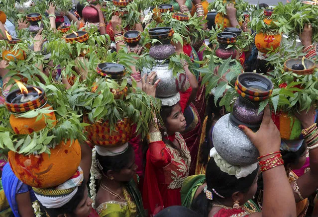 Indian women carry on their heads, pots filled with cooked rice decorated with turmeric and neem leaves as a ritual offering to the Hindu goddess Kali during the “Bonalu” festival in Hyderabad, India, Sunday, July 28, 2019. Bonalu is a month-long Hindu folk festival of the Telangana region dedicated to Kali, the Hindu goddess of destruction. (Photo by Mahesh Kumar A./AP Photo)