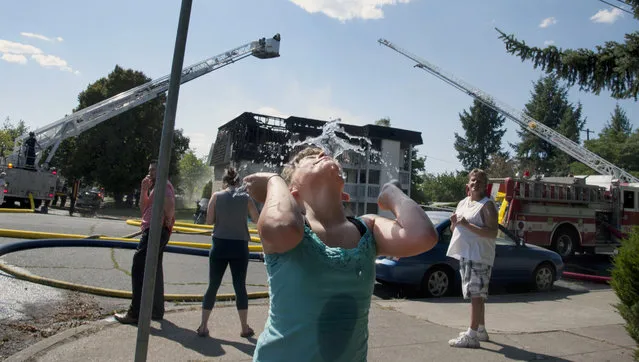Jalesa Keen, 8, splashes herself with water from a fire hydrant as the Spokane Fire Department battles a three-alarm apartment fire Thursday, July 2,2015, in Spokane, Wash. From Seattle to Salt Lake City, the West is baking under record heat. Temperatures reaching the triple digits have made fire conditions extreme and sent folks looking for relief heading into the Fourth of July weekend. (Photo by Dan Pelle/The Spokesman-Review via AP Photo)