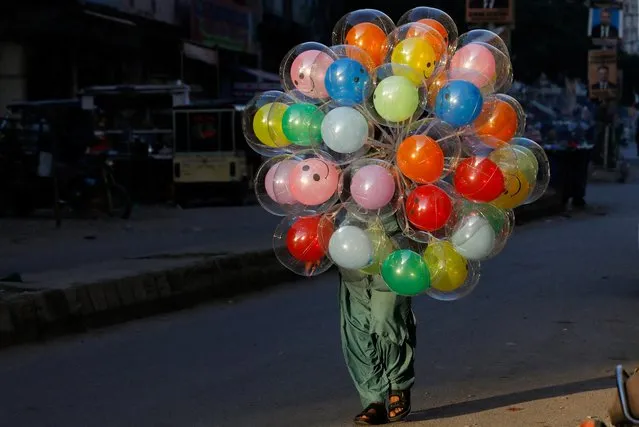 Veshu, 25, whose family moved to Karachi from Pakistan's southeastern desert area of Tharparkar to look for work, carries a bunch of balloons while selling them along a street in Karachi, Pakistan on January 27, 2022. (Photo by Akhtar Soomro/Reuters)