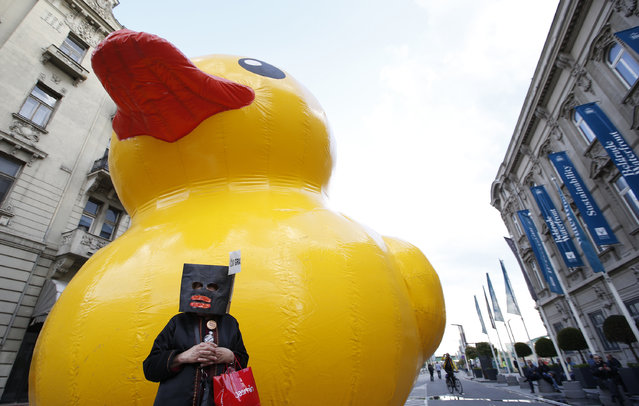 A woman wearing a mask stands in front of a giant yellow rubber duck, a mascot of a group of people criticizing the Belgrade waterfront plan, during a protest in Belgrade, Serbia, Tuesday, April 25, 2017. Several thousand people have rallied in the Serbian capital, Belgrade, one year after a mysterious demolition in an area marked for a United Arab Emirates-financed real estate project. (Photo by Darko Vojinovic/AP Photo)