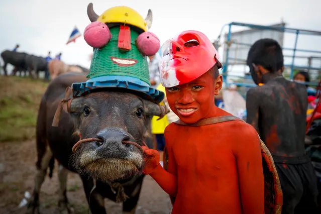 A young Thai boy painted and wearing a costume poses next to a buffalo before the buffalo parade during the annual water buffalo races in Chonburi province, Thailand, 23 October 2018. Around three hundred buffalos take part in the centuries old water buffalo racing festival, divided into categories according to the buffalo's age. The anual festival is held every October among rice farmers to celebrate the rice harvest and mark the end of the Buddhist Lent. (Photo by Diego Azubel/EPA/EFE)