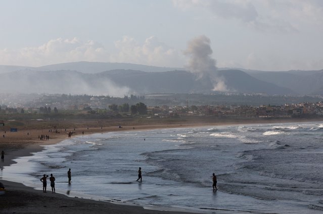 People walk at a beach as smoke billows over southern Lebanon following Israeli strikes, amid ongoing cross-border hostilities between Hezbollah and Israeli forces, as seen from Tyre, southern Lebanon on September 23, 2024. (Photo by Aziz Taher/Reuters)