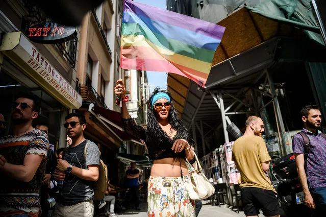 A woman holding rainbow flag look on as Turkish anti-riot police officers fire rubber bullets to disperse demonstrators gathered for a rally staged by the LGBT community on Istiklal avenue in Istanbul on June 19, 2016. Turkish riot police fired rubber bullets and tear gas to break up a rally staged by the LGBT community in Istanbul on June 19 in defiance of a ban. Several hundred police surrounded the main Taksim Square – where all demonstrations have been banned since 2013 – to prevent the “Trans Pride” event taking place during Ramadan. (Photo by Ozan Kose/AFP Photo)