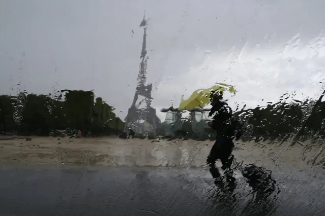 Rain drops on a car window distort the Eiffel Tower as a woman takes shelter under a yellow umbrella during a rain shower in Paris May 13, 2014. (Photo by Gonzalo Fuentes/Reuters)