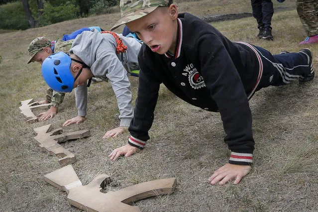 In this photo taken on Friday, July 14, 2017, students at a paramilitary camp for children do push-ups outside Kiev, Ukraine. As the deadly conflict in eastern Ukraine entered its third year, some parents in Ukraine are anxious to make sure their children are ready to fight it, instead of swimming and playing volleyball. (Photo by Efrem Lukatsky/AP Photo)