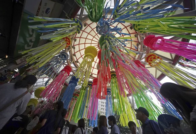 People walk under colorful paper streamers for the Tanabata Star Festival at a shopping arcade at Asagaya in Tokyo Saturday, August 5, 2017. According to legend, deities Orihime (Vega) and her lover Hikoboshi (Altair), separated by the Milky Way, are allowed to meet only once a year during this period. People celebrate the festival by writing wishes on strips of paper and hanging them under bamboo trees. (Photo by Eugene Hoshiko/AP Photo)
