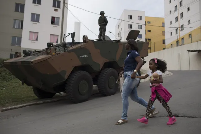 A girl and her mother walk past an army armored vehicle at the Caramujo slum in Niteroi, Brazil, Wednesday, August 16, 2017. (Photo by Leo Correa/AP Photo)