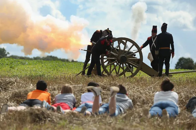 Local children lie in the grass as they watch historical society members fire five volleys of a cannon at the inauguration ceremony of a monument to honour members of the British Cheshire Regiment and other soldiers who died fighting the German Army exactly 100 years before at the same site during World War I on August 24, 2014 in Audregnies, Belgium. (Photo by Sean Gallup/Getty Images)