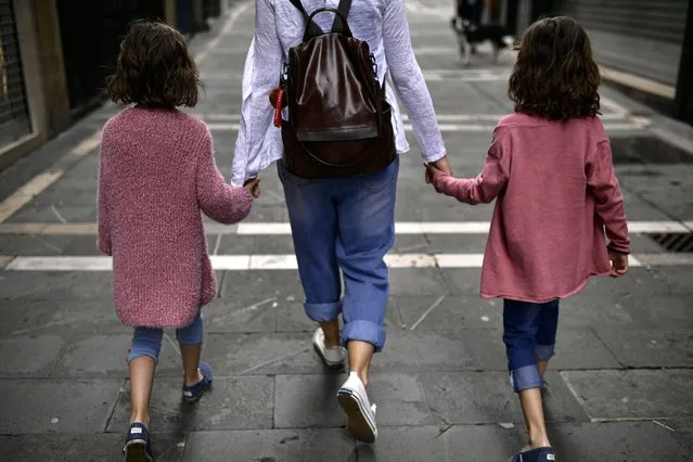 A family go for a walk taking their hands along a street of the old city, in Pamplona, northern Spain, Sunday, April 27, 2020. On Sunday, children under 14 years old will be allowed to take walks with a parent for up to one hour and within one kilometer from home, ending six weeks of compete seclusion. (Photo by Alvaro Barrientos/AP Photo)
