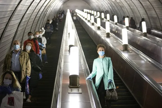 People wearing face masks and gloves to protect against coronavirus, observe social distancing guidelines as they go down the subway on the escalator in Moscow, Russia, Tuesday, May 12, 2020. From Tuesday onward, wearing face masks and latex gloves is mandatory for people using Moscow's public transport. President Vladimir Putin on Monday declared an end to a partial economic shutdown across Russia due to the coronavirus pandemic, but he said that many restrictions will remain in place. (Photo by Alexander Zemlianichenko/AP Photo)