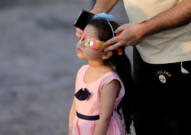 A girl uses solar viewers to watch a partial solar eclipse in Mumbai, India on October 25, 2022. (Photo by Niharika Kulkarni/Reuters)