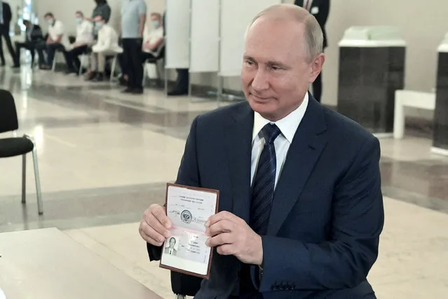 Russian President Vladimir Putin shows his passport to a member of an election commission as he arrives to take part in voting at a polling station in Moscow, Russia, Wednesday, July 1, 2020. The vote on the constitutional amendments that would reset the clock on Russian President Vladimir Putin's tenure and enable him to serve two more six-year terms is set to wrap up Wednesday. (Photo by Alexei Druzhinin, Sputnik, Kremlin Pool Photo via AP Photo)