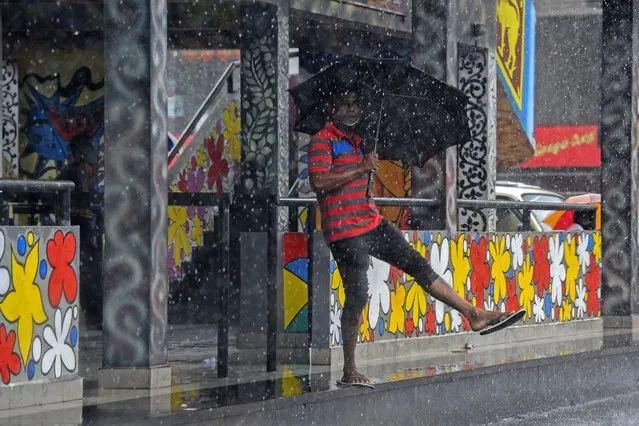 A local resident shelters under an umbrella during a downpour in Colombo's suburb of Dompe on July 20, 2020. (Photo by Ishara S. Kodikara/AFP Photo)