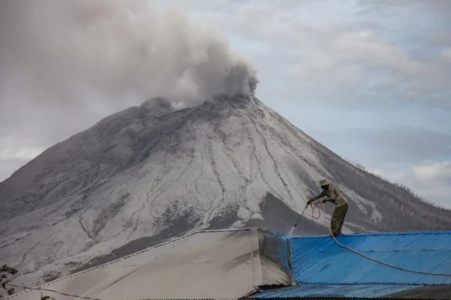 A villager cleans volcanic ash from his roof at Naman Teran village in Karo, North Sumatra, on August 11, 2020 a day after the eruption of Mount Sinabung (background). (Photo by Ivan Damanik/AFP Photo) 