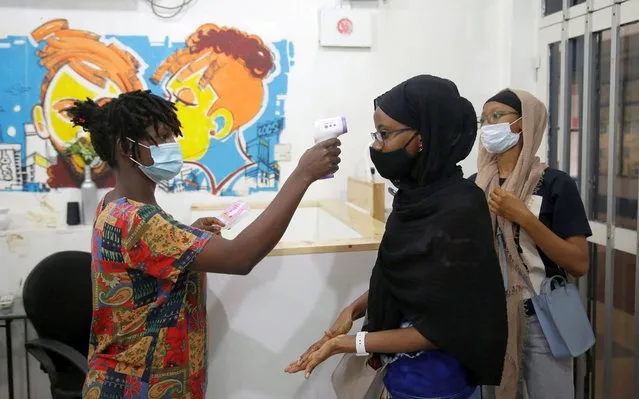 A hair stylist wearing a face mask to protect against coronavirus uses a thermometer to take the temperature of a customer inside a salon in Lagos, Nigeria, Friday September 18, 2020. Nigeria officials recently reopened worship centres and international flights following months of closure to curb the spread of coronavirus. (Photo by Sunday Alamba/AP Photo)