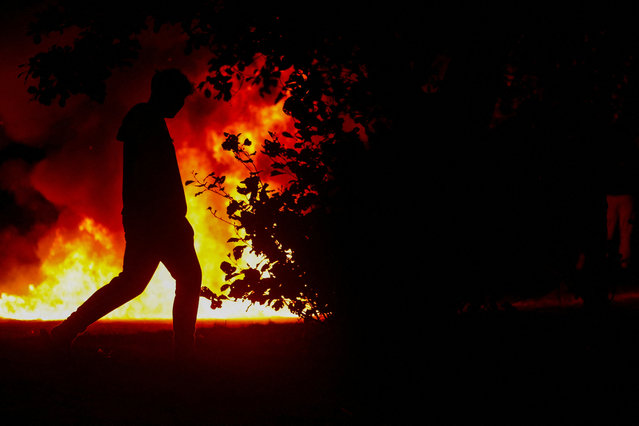 A person walks as flames rise during a the second night of riots, in Ballymena, Northern Ireland, on June 10, 2025. (Photo by Clodagh Kilcoyne/Reuters)