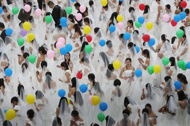 Women in wedding dresses hold balloons at a wedding dress market during an event attempting to break the Guinness world record for a gathering with the most people dressed as brides, in Suzhou, Jiangsu Province, China, October 7, 2016. (Photo by Reuters/China Daily)