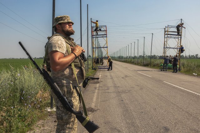 A Ukrainian serviceman stands guard with a shotgun as his fellow soldiers install anti-drone nets over a road at an undisclosed location in the eastern Donetsk region on July 8, 2025, amid the Russian invasion of Ukraine. (Photo by Roman Pilipey/AFP Photo)