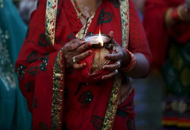 A devotee holding offerings and oil lamp on her hand offers prayers to the setting sun during the "Chhat" festival at Bagmati river in Kathmandu, Nepal November 17, 2015. (Photo by Navesh Chitrakar/Reuters)