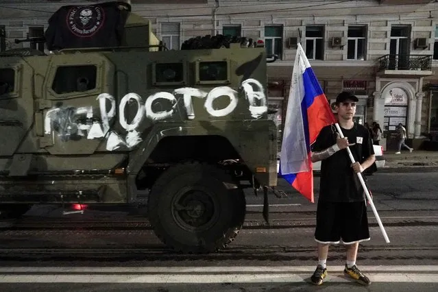 A man holds the Russian national flag in front of a Wagner group military vehicle with the sign read as “Rostov” in Rostov-on-Don late on June 24, 2023. Rebel mercenary leader Yevgeny Prigozhin who sent his fighters to topple the military leaders in Moscow will leave for Belarus and a criminal case against him will be dropped as part of a deal to avoid “bloodshed”, the Kremlin said on June 24. (Photo by AFP Photo/Stringer)