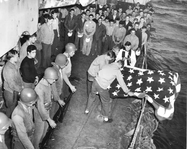 In this handout from the U.S. Coast Guard, the flag-draped bodies of two Navy men who died from wounds suffered in the Battle of Iwo Jima, are buried at sea from the deck of a Coast Guard invasion transport off the coast of Iwo Jima, April 6, 1945. The ship's chaplain reads the burial rites over the deceased as their comrades stand silently, some with heads bowed. The bodies are slipped over the side from beneath the flag for which these heroes gave their lives. (Photo by AP Photo/U.S. Coast Guard)