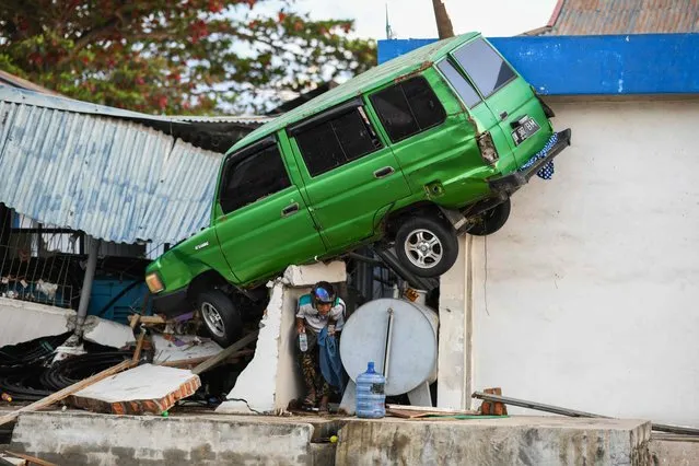 A survivor walks under a car struck on a building in Palu, Indonesia' s Central Sulawesi on October 1, 2018, after an earthquake and tsunami hit the area on September 28. Indonesian volunteers began burying bodies in a mass grave with space for more than a thousand people on October 1, victims of a quake- tsunami that devastated swathes of Sulawesi and left authorities struggling to deal with the sheer scale of the disaster. (Photo by Jewel Samad/AFP Photo)
