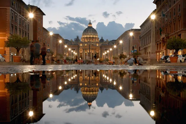 This photo taken on September 1, 2018 shows the St Peter' s Basilica reflected in a puddle as tourists walk along the Via della Conciliazione in Rome. (Photo by Tiziana Fabi/AFP Photo)