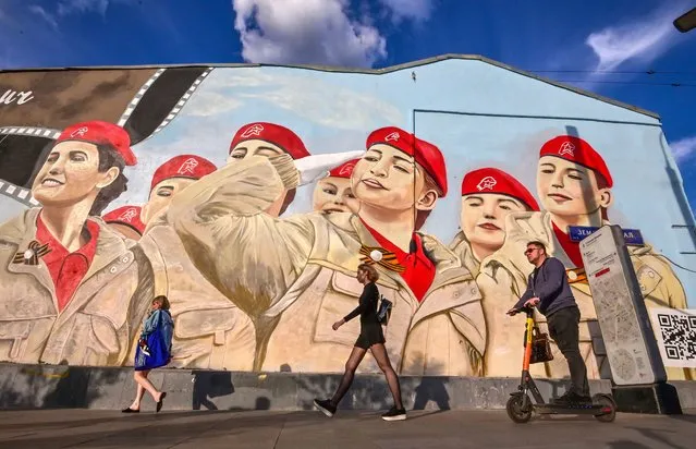 Pedestrians walk past a wall of a house with huge graffiti depicting members of the Russian patriotic youth movement Yunarmiya in Moscow, on May 25, 2021. (Photo by Yuri Kadobnov/AFP Photo)