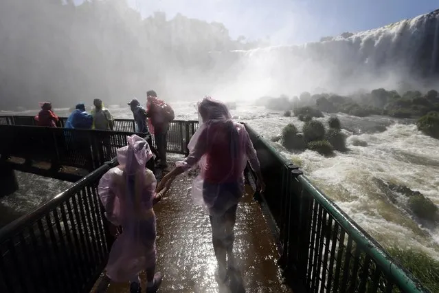 In this photo taken Sunday, March 15, 2015, tourists wear plastic ponchos as they walk in the spray of Iguazu Falls, in Foz do Iguazu, Brazil. Iguazu Falls, on the border of Argentina and Brazil, is part of the Guarani Aquifer, one of the world's major underground reserves of fresh water. (Photo by Jorge Saenz/AP Photo)