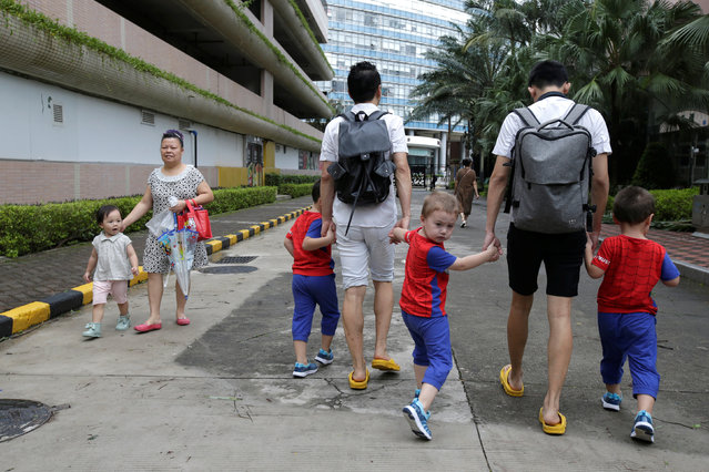 A girl looks at An Hui (L) and his partner Ye Jianbin walking with their sons, An Zhizhong, An Zhiya and An Zhifei at a residential community in Shenzhen, Guangdong province, China September 17, 2018. The triplets were conceived with the help of a German egg donor. (Photo by Jason Lee/Reuters)