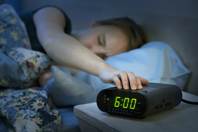 Young woman pressing snooze button on early morning digital alarm clock radio. (Photo by Elenathewise/Getty Images/iStockphoto)