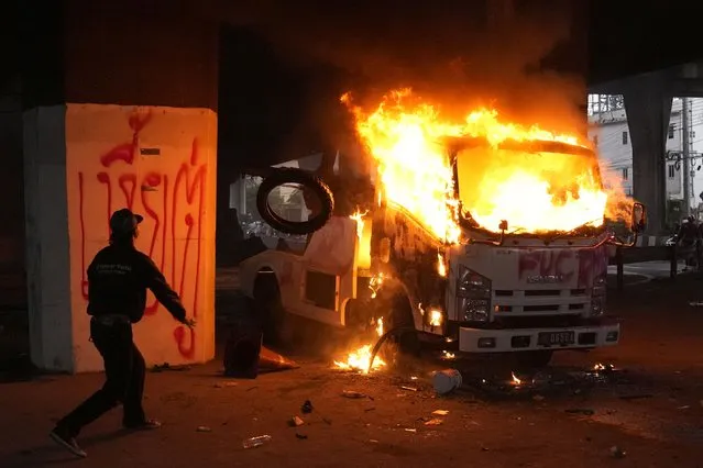 Anti-government protester throw tires into a burning police truck during protest in Bangkok, Thailand, Wednesday, August 11, 2021. (Photo by Sakchai Lalit/AP Photo)