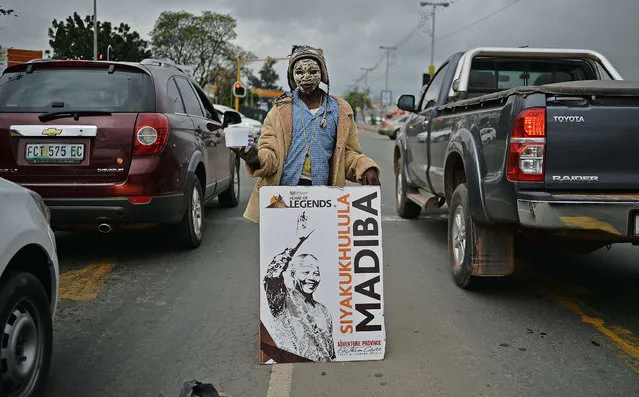 A street child holds up a poster bearing the image of South African former president Nelson Mandela as he begs during rush hour in Mthata near Nelson Mandela's former home Qunu on December 9, 2013. Qunu, the village where Mandela grew up will be his final resting place on December 15, 2013 when he is buried. (Photo by Carl de Souza/AFP Photo)