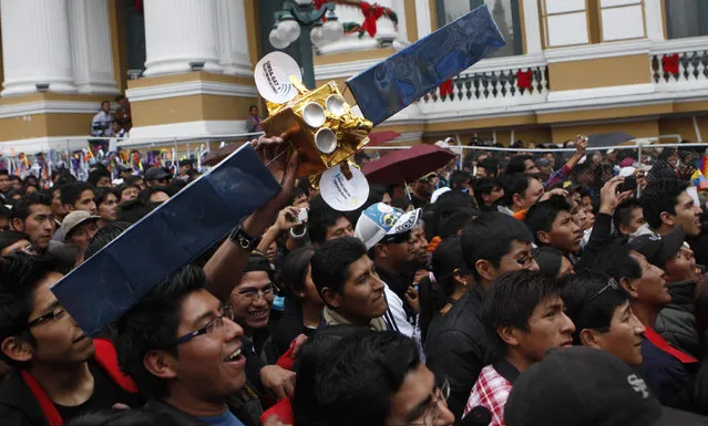 A man holds a miniature replica of the country's first telecommunications satellite during the live broadcast from China of the launch, in La Paz, Bolivia, Friday, December 20, 2013. (Photo by Juan Karita/AP Photo)