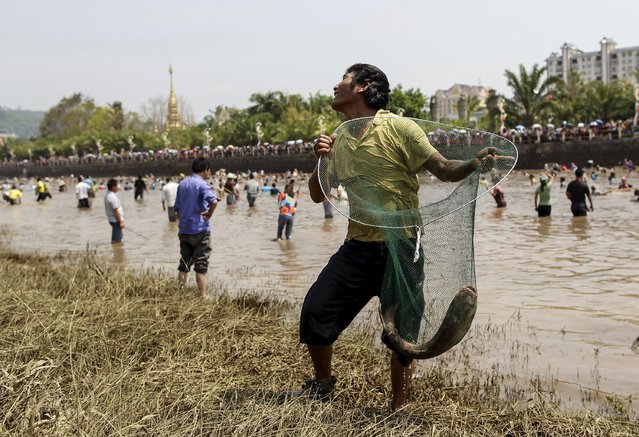A man catches a fish with a net as he stands by the riverside during the Holy Fish Festival, in Menglian Dai, Lahu and Va Autonomous County, Yunnan province April 12, 2015. Thousands of people will get down the Nanlei River in Menglian to catch fish during the festival which is celebrated on April 12 every year. (Photo by Wong Campion/Reuters)