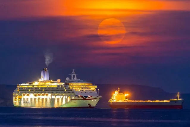 The Harvest Moon is obscured by thin high clouds as it rises up from behind the P&O cruise ship Aurora and the Lemessos Castle bulk carrier which are anchored in the bay at Weymouth in Dorset, United Kingdom the on the last day of astronomical summer on September 21, 2021. (Photo by Graham Hunt/Alamy Live News)