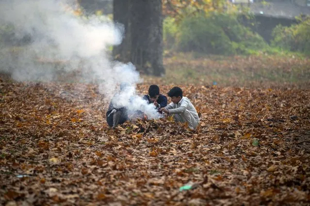 Kashmiri boys warm their hands over the burning China leaves on the outskirts of Srinagar, Indian controlled Kashmir, Sunday, November 14, 2021. Kashmiris collect fallen leaves in autumn to make charcoal for use during winters. (Photo by Mukhtar Khan/AP Photo)